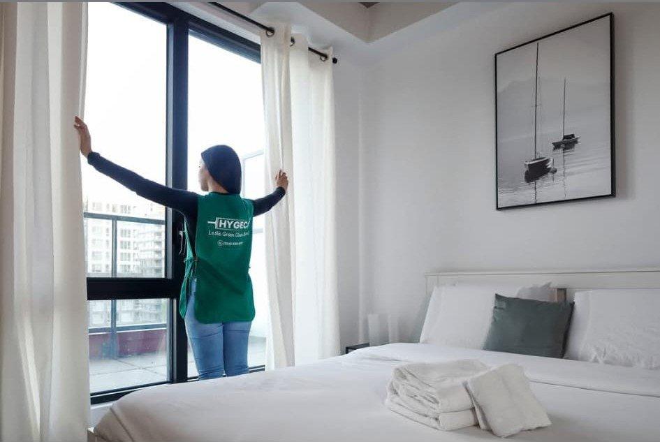 Employée Hygeco ouvrant les rideaux d’une chambre propre et lumineuse